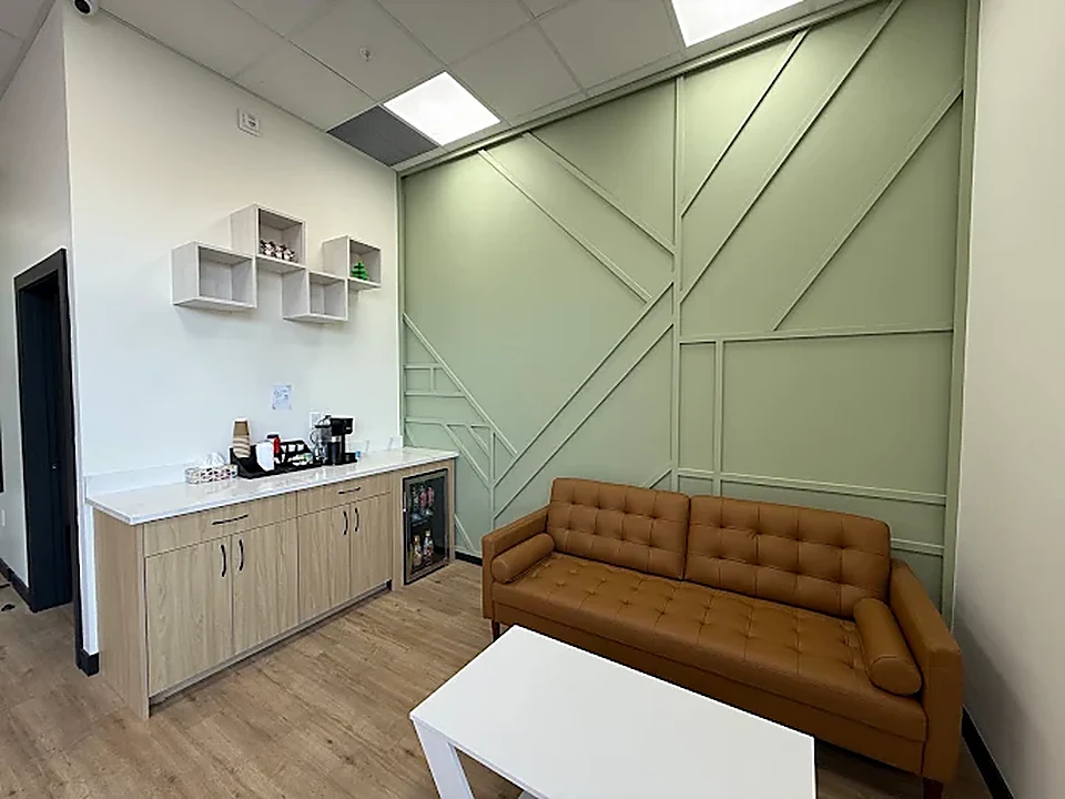 Patient waiting lounge at Capilano Mall Dental with leather sofa, sage-green feature wall and complimentary refreshment counter