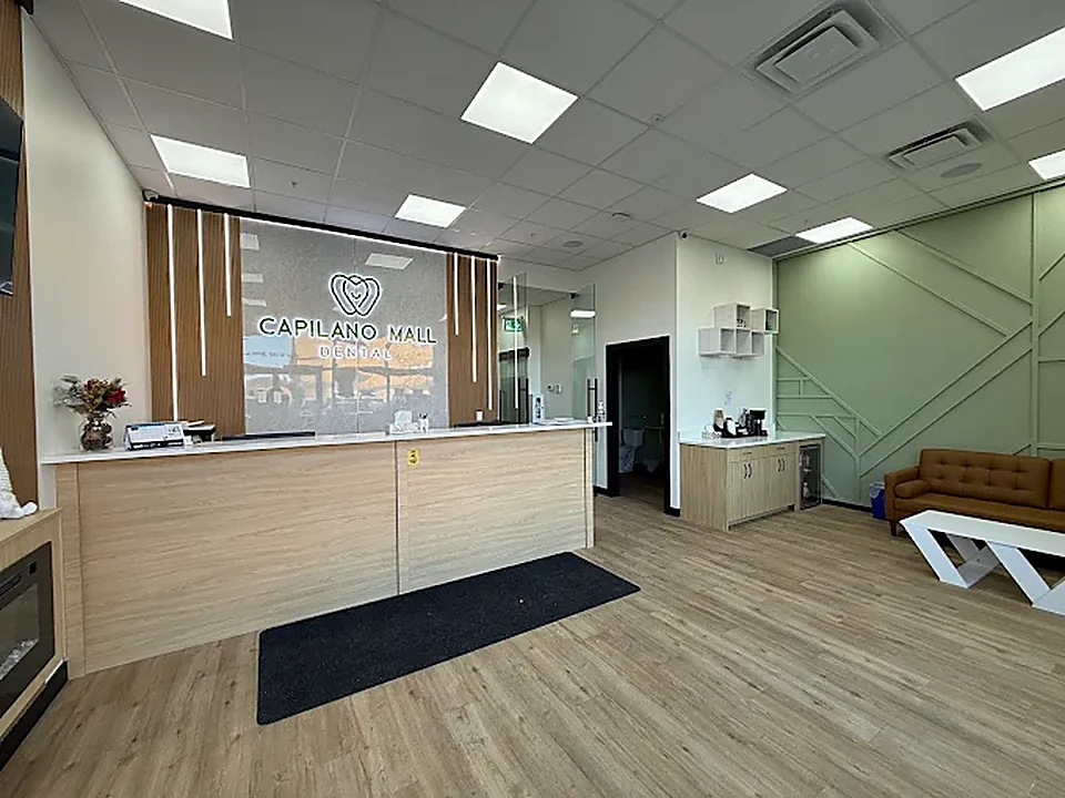 Reception desk and patient lounge at Capilano Mall Dental, with sage-green feature wall and leather seating